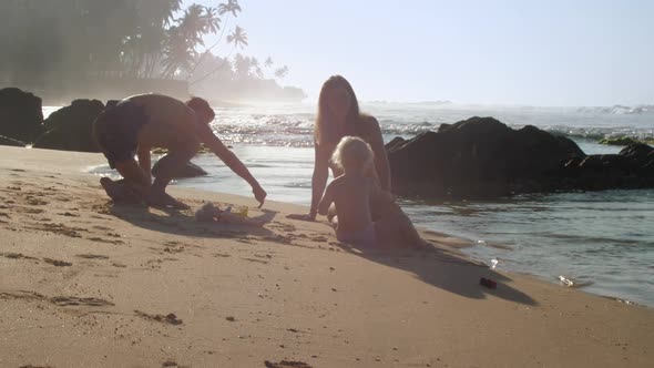 Family Enjoys Rest Sitting on Beach and Playing with Child alt