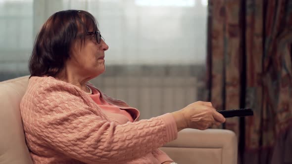 Grandmother With TV Remote Watching TV And Channel Surfing. Senior Woman Using TV Remote Control. alt