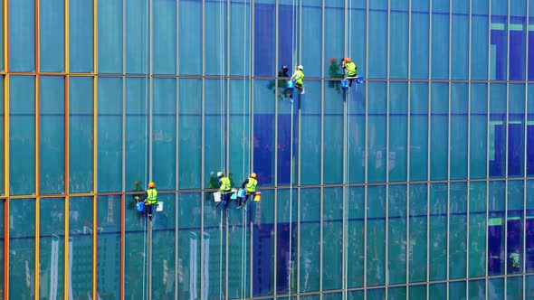 Five Men Workers in Red and Yellow Work Clothes Cleaning the Exterior Windows of a Business alt