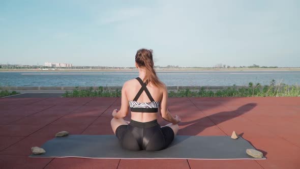 Athletic Woman Sitting in lotus position and Doing Yoga on Lake Background alt