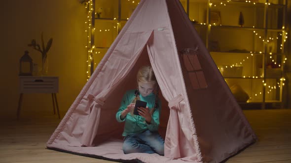 Child Working with Cellphone in Teepee Tent at Night alt