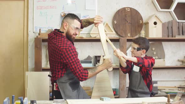Father and Son Playing Knights with Wooden DIY Swords at Carpenter Workshop