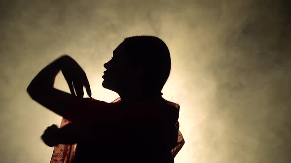 Silhouette a Young Girl Dancer in a Red Sari. Indian Folk Dance. Shot in a Dark Studio with Smoke alt