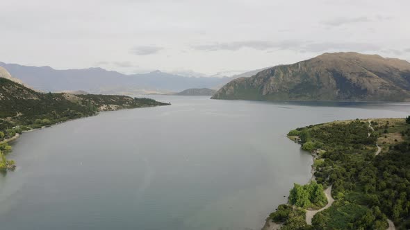 Aerial tracking down lake Wanaka on a still cloudy morning in central Otago as the mountains sit in alt