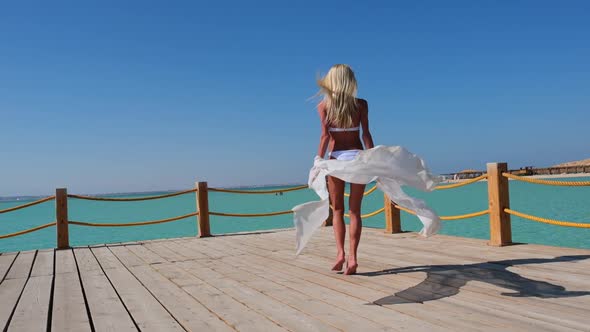 Pretty Young Woman in White Pareo Standing on Pier Near Sea alt