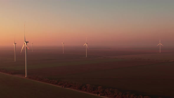 Wind Driven Generators Rotate in Rural Field at Sunset