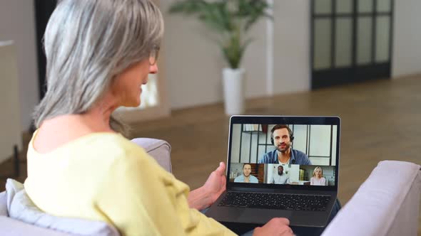 Contemporary Senior Woman Sitting on Armchair and Using Laptop for Video Connection alt