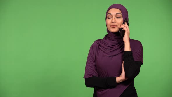 A Young Beautiful Muslim Woman Talks on a Smartphone with a Smile  Green Screen Background