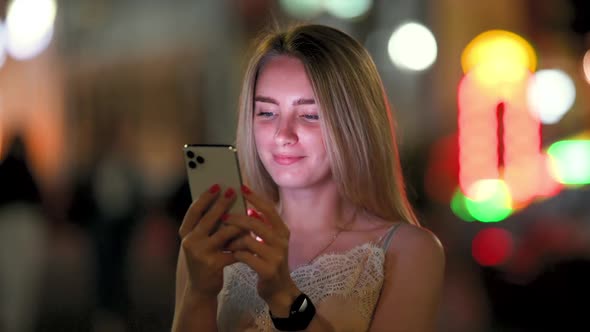 Woman Messaging on Phone at Night on the Street With the Lights of the Road Blurred Background