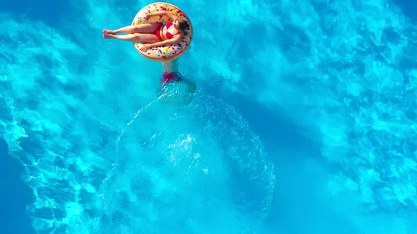 Aerial View of Man Dives Into the the Pool While Girl is Lying on a Donut Pool Float alt
