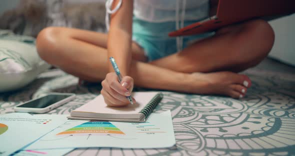 Middle Shot of a Woman Working at Home She Sits on the Cozy Carpet and Writes Notes at Notepad alt