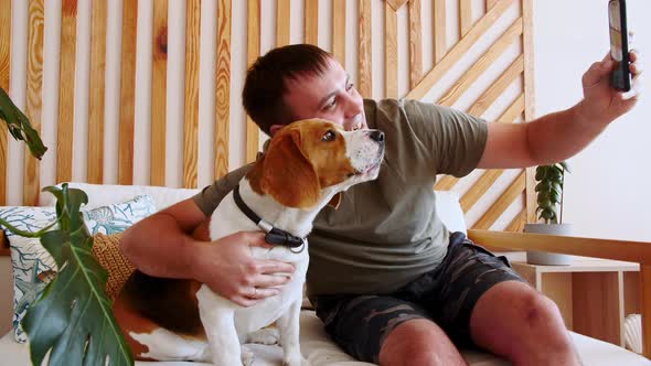 A Joyful Young Man Sitting at Table and Hugging Her Dog Beagle While Making Video Call alt