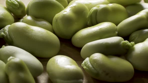 Slider shot from left to right at extreme close up of a pile of sweating, backlit, green fava beans alt