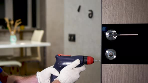 Installing A Lock On The Front Door. A Carpenter In A Special Uniform Repairs The Lock alt