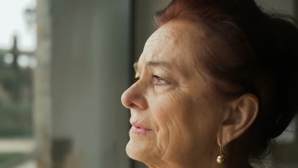 sad worry old woman looking out the window: elderly depressed woman portrait