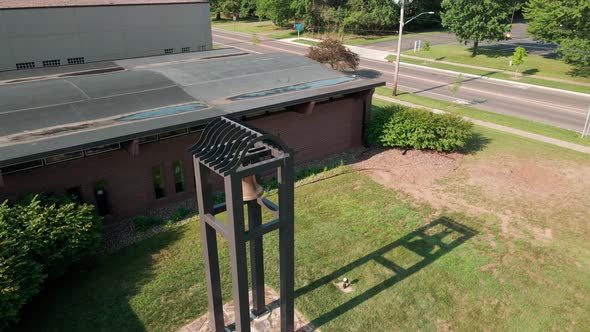 Aerial view of bell outside of church building. Sturdy steel posts casting shadows on the grass.