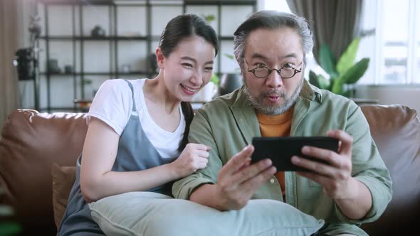 exited asian marry couple enjoy playing smartphone game online mobile together