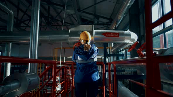 Woman worker in a factory in a helmet and uniform rotates a huge red valve alt