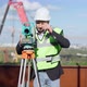 Portrait of Positive Professional Male Engineer Using Theodolite Outdoors Taking Off Hard Hat - VideoHive Item for Sale