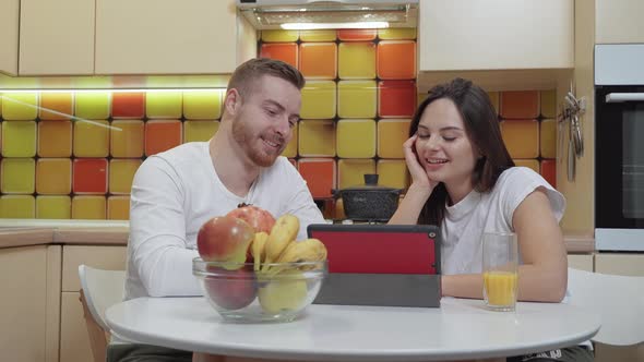 Young couple looking together something on the tablet at the kitchen table