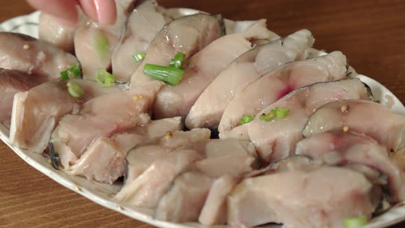 Pieces of Fish in Oil Lie on a Plate a Woman's Hand Sprinkles Them alt