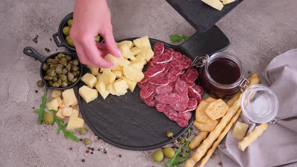 Making Meat and Cheese Antipasto Plater Woman Putting Pieces of Parmesan Hard Cheese on Stone alt