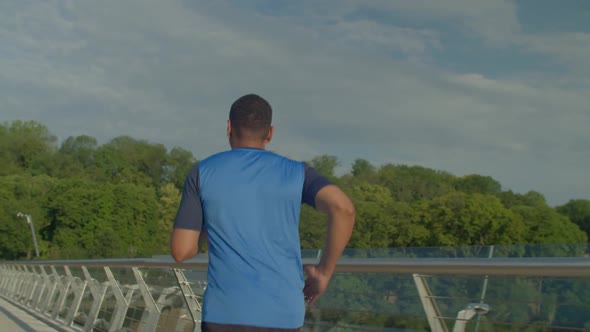 Rear View of Sporty Fitness African American Man Jogging on Bridge at Dawn alt