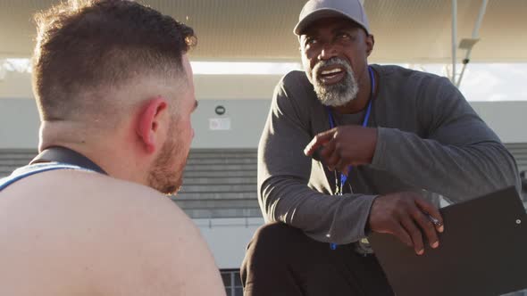 African american male coach and caucasian male athlete sitting and ...