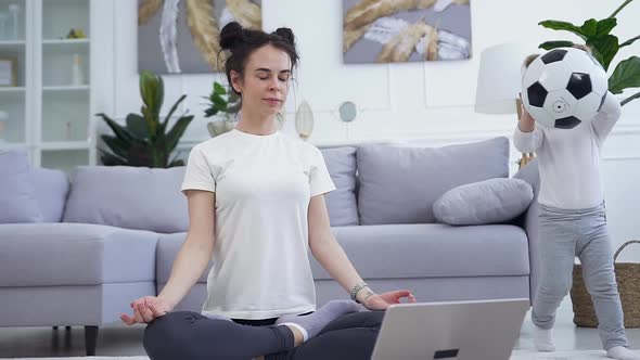 Woman Sitting on the Floor on Lotus Pose while Her Energetic Beautiful Small Daughter Playing  alt