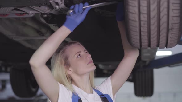 Portrait of Young Caucasian Woman Standing Under Car and Tightening Screws on Wheel. Female Auto alt