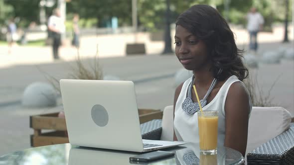 Young African Woman Sitting Alone in a Cafe Having a Videoconferance on a Laptop alt