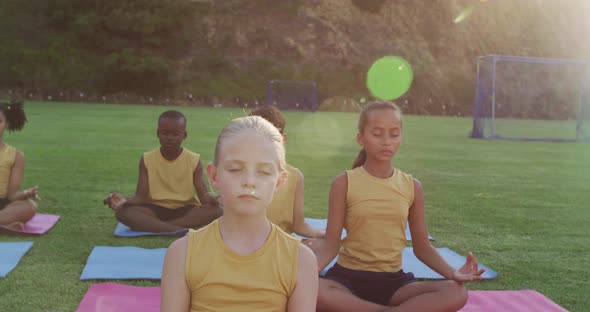 Diverse group of schoolchildren sitting on mats meditating during yoga lesson outdoors alt