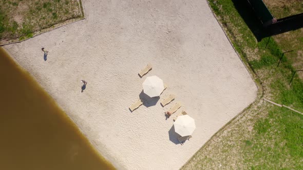 People Taking Rest at the Beach Area with Sand and Loungers Near a Small Lake in a Cottage Village alt