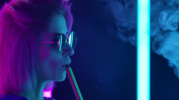 Portrait of a Young Stylish Woman in Sunglasses Smoking a Hookah and Blowing Out Puffs of Smoke alt