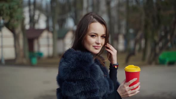 Beautiful woman with a plastic cup of coffee in the park alt