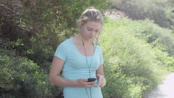 A young woman runner putting on earbuds before going on a run. alt