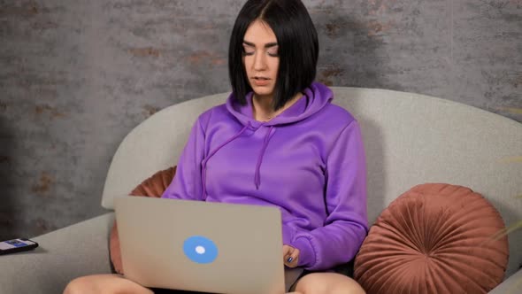 Young Woman Receives Notification on Laptop but Answers on Mobile Phone alt