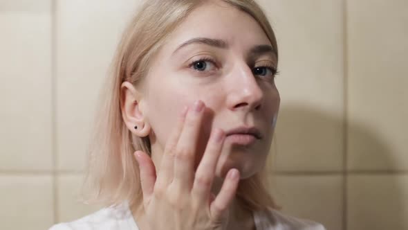 Woman applying cream on her face in bathroom.