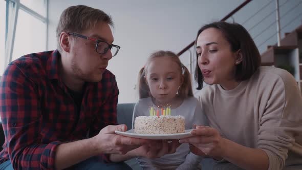 Young Cheerful Daughter Is Blowing Candles on White Birthday Cake with Family at Home. alt