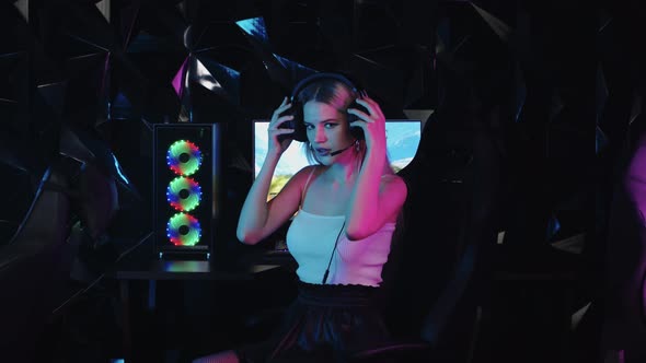 Young Blonde Sexy Gamer Girl Putting on Headphones and Starts Playing the Game alt