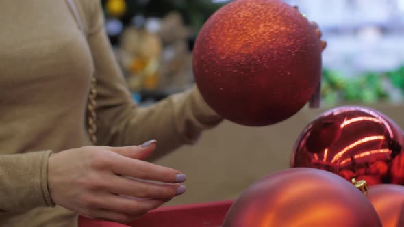 Young Woman Hands Take Glittering Bauble of Red Colour alt