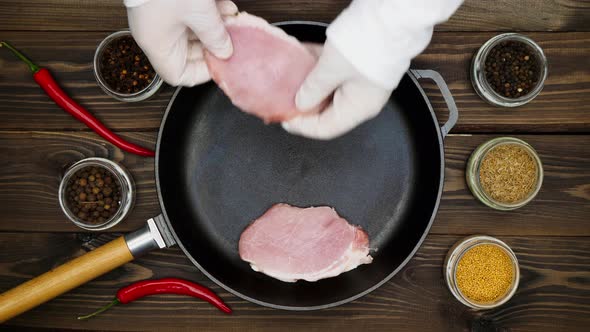 The cook puts the meat on the pan. Sliced pork steaks in a cast iron skillet. Black peppercorns