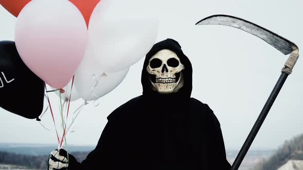 Death with a Scythe Holds Balloons and Hides Behind Them, but Then Shows a Creepy Face That Laughs alt