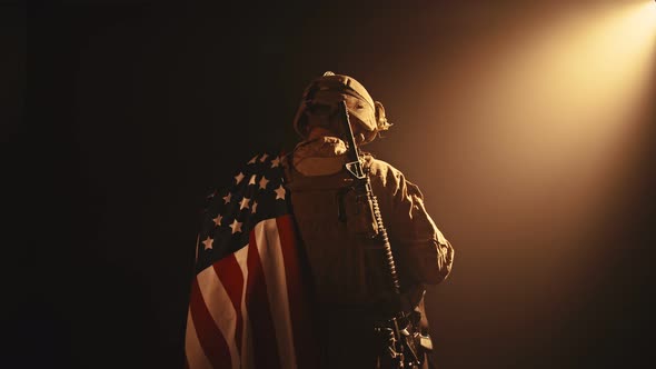 USMC Soldier Standing with His Back to Us in the Dark Holding USA National Flag alt