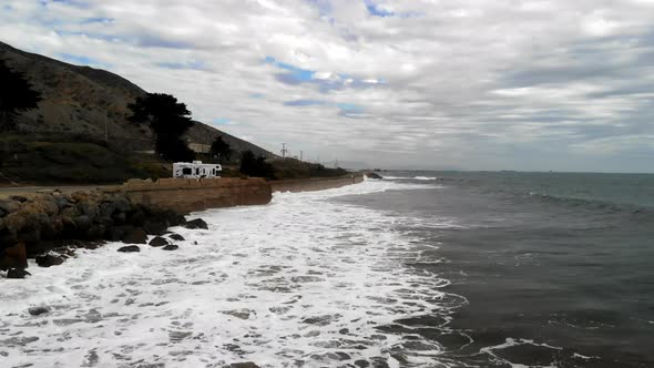Aerial drone shot on a cloudy day over the Pacific Ocean waves next to RV campers and the cliffs alo alt