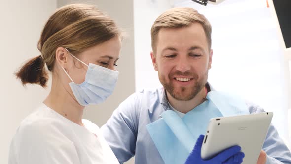 Female Orthodontist Advises a Young Man in the Dental Office a Doctor Holding a Tablet alt