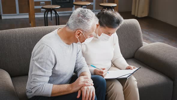 Senior Man and Woman in Protective Masks Filling Out an Agreement Form for All Kinds of Tests at alt