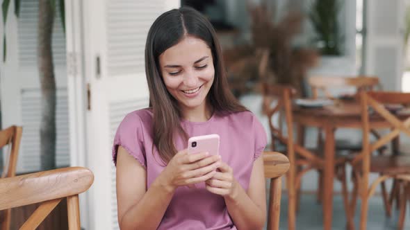 Portrait of Happy Woman Sitting in Cafe and Using Mobile Phone, Laughing alt