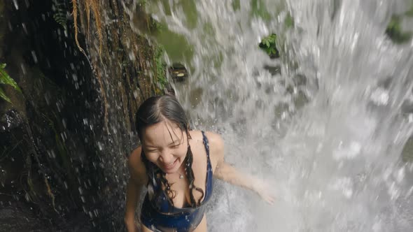 A Young Korean Woman in a Blue Swimsuit Walks Through a Large Wall of Falling Water on a Mountain