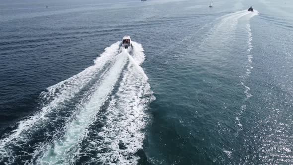 A large white boat is moving at speed on the blue sea water. alt